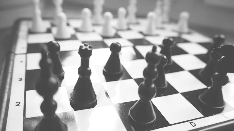 Chess board with black pieces in sharp focus in the foreground and white pieces blurred behind, shot from a low angle