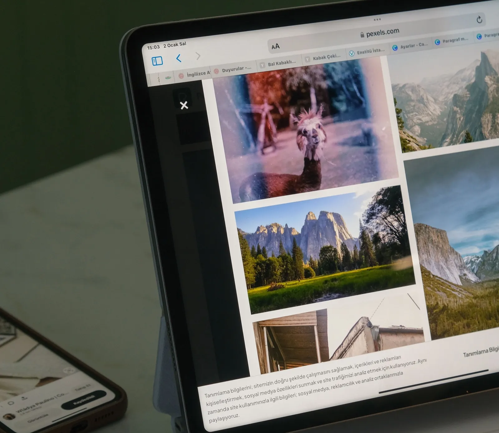 Person's hands on a white keyboard typing while viewing a tablet displaying the Pexels website with a gallery of landscape and nature shots including mountains, valleys, and scenic views